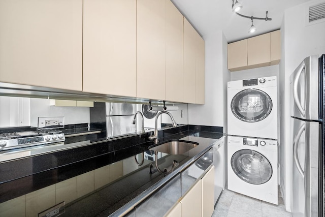 interior space with sink, cream cabinets, stainless steel refrigerator, and stacked washer / dryer