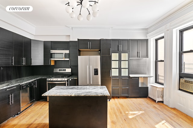 kitchen featuring appliances with stainless steel finishes, backsplash, light stone countertops, a kitchen island, and radiator heating unit