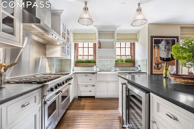 kitchen featuring pendant lighting, wall chimney range hood, beverage cooler, and range with two ovens