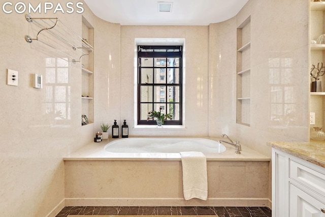 bathroom featuring vanity, a relaxing tiled tub, and built in shelves