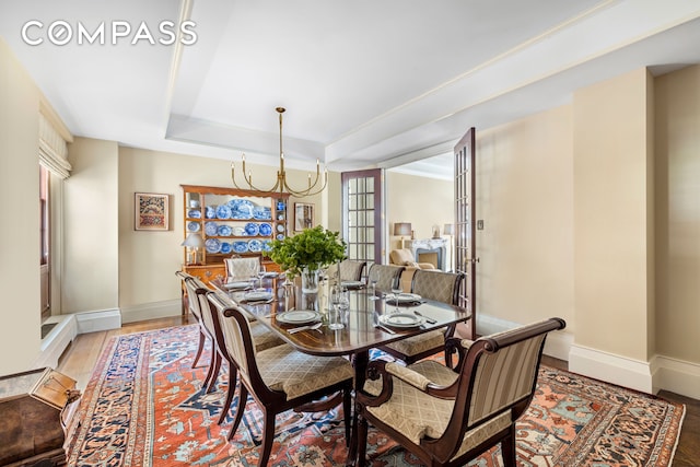 dining area featuring light wood-style floors, baseboards, a raised ceiling, and an inviting chandelier