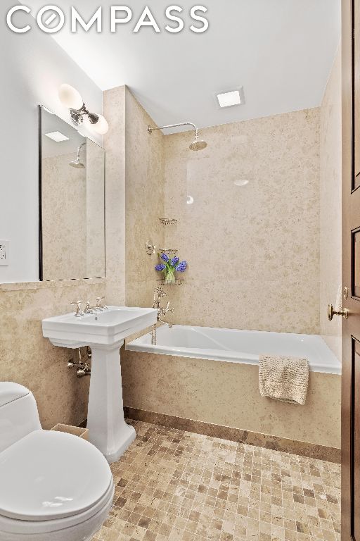 bathroom with toilet, tiled shower / bath, and tile walls