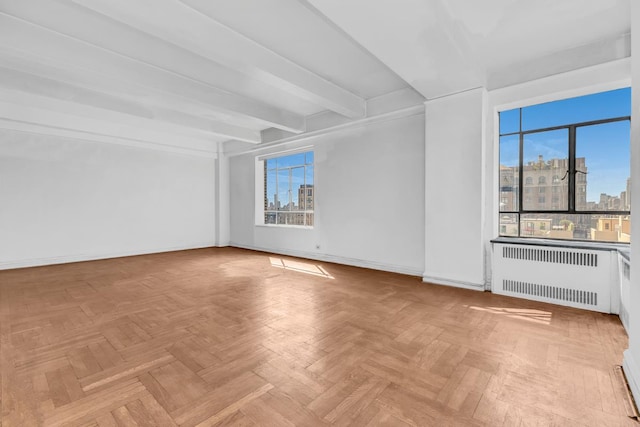 spare room with baseboards, a city view, radiator, and beam ceiling