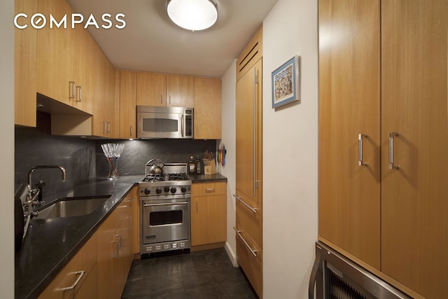 kitchen with stainless steel appliances, a sink, backsplash, and dark stone counters