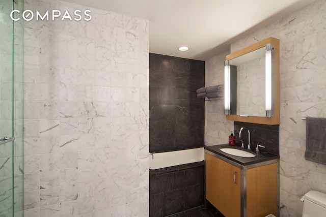 bathroom with toilet, vanity, a tile shower, and tile walls