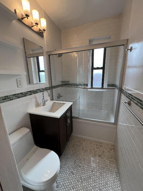 full bathroom featuring toilet, enclosed tub / shower combo, tile walls, tile patterned floors, and vanity