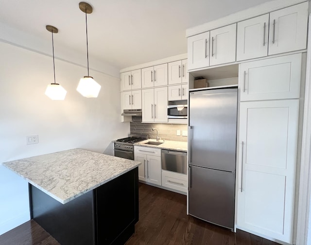 kitchen with premium appliances, light stone counters, a sink, white cabinets, and pendant lighting