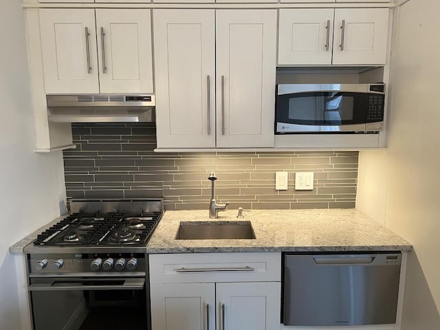 kitchen with white cabinetry, stainless steel appliances, decorative backsplash, sink, and light stone counters