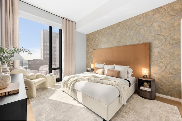 bedroom with wallpapered walls, an accent wall, baseboards, and wood finished floors