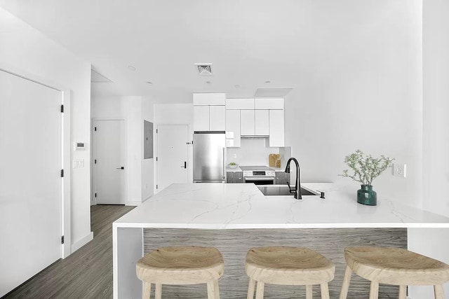 kitchen featuring appliances with stainless steel finishes, a sink, a peninsula, white cabinets, and a breakfast bar
