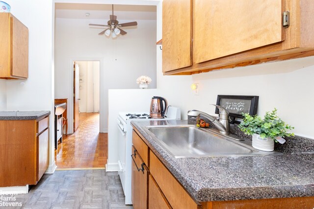 kitchen featuring ceiling fan, dark parquet flooring, sink, and white gas range oven