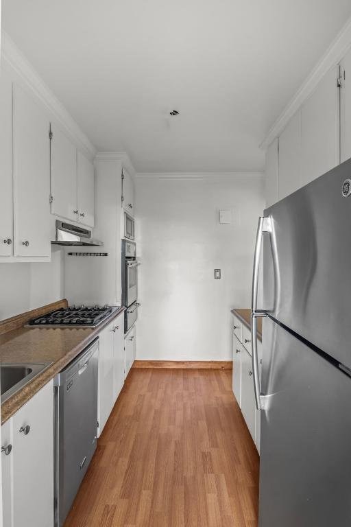 kitchen with appliances with stainless steel finishes, crown molding, white cabinetry, and light hardwood / wood-style floors