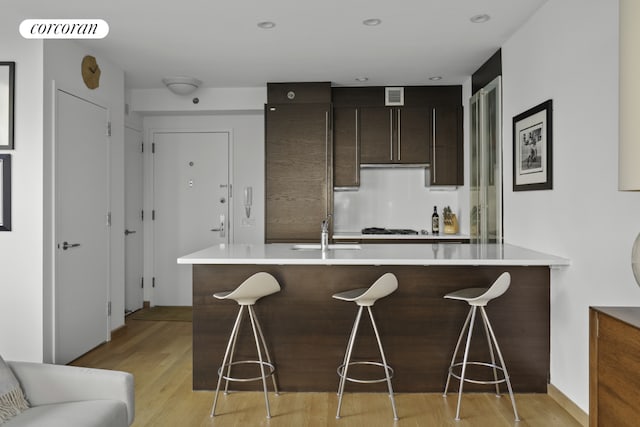 kitchen featuring gas cooktop, sink, light wood-type flooring, a breakfast bar area, and dark brown cabinets