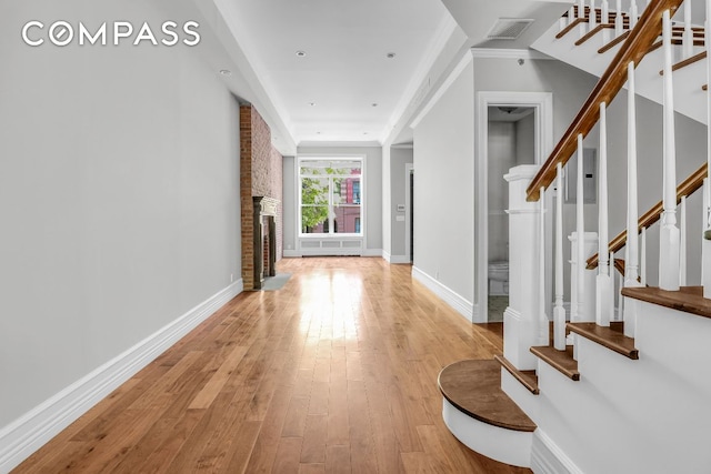 entrance foyer featuring a brick fireplace, ornamental molding, and light wood-type flooring