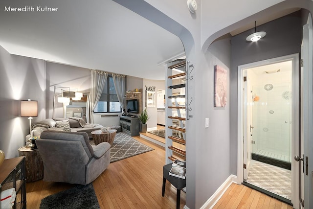 living area with baseboards, wood-type flooring, and arched walkways