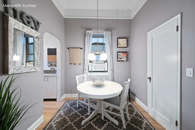 dining area with cooling unit, baseboards, arched walkways, and light wood finished floors