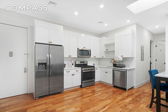 kitchen featuring light wood finished floors, open shelves, stainless steel appliances, light countertops, and visible vents