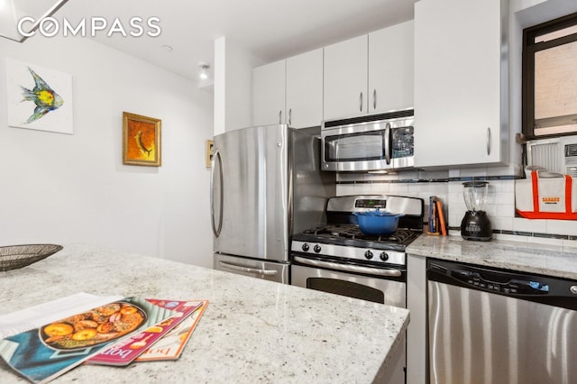 kitchen with light stone countertops, appliances with stainless steel finishes, white cabinets, and backsplash