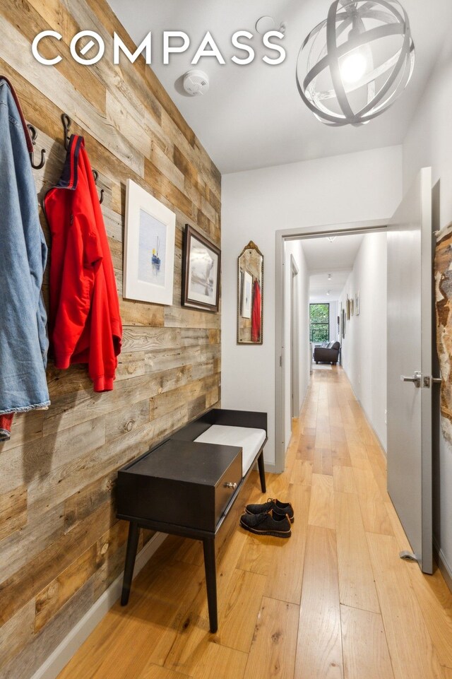 hallway with wooden walls, a chandelier, and light wood-type flooring
