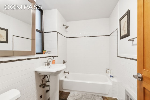 full bath with toilet, a sink, visible vents, tile walls, and shower / washtub combination