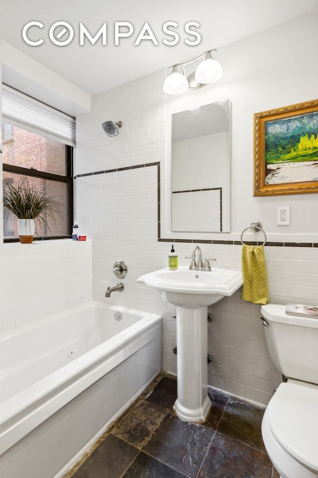 full bathroom featuring stone tile flooring, toilet,  shower combination, and tile walls