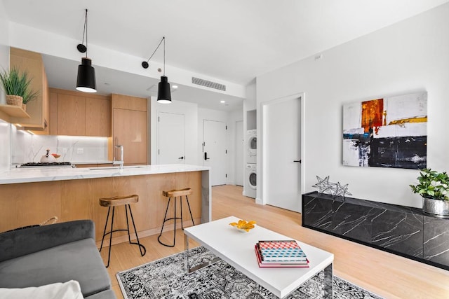 living room with light hardwood / wood-style floors, sink, and stacked washing maching and dryer