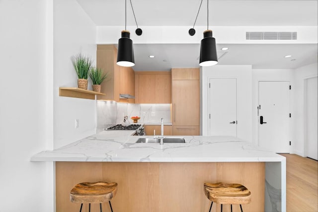 kitchen featuring a breakfast bar area, a sink, visible vents, hanging light fixtures, and light stone countertops