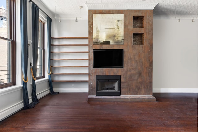 unfurnished living room with dark wood-type flooring, baseboards, a fireplace with raised hearth, and track lighting