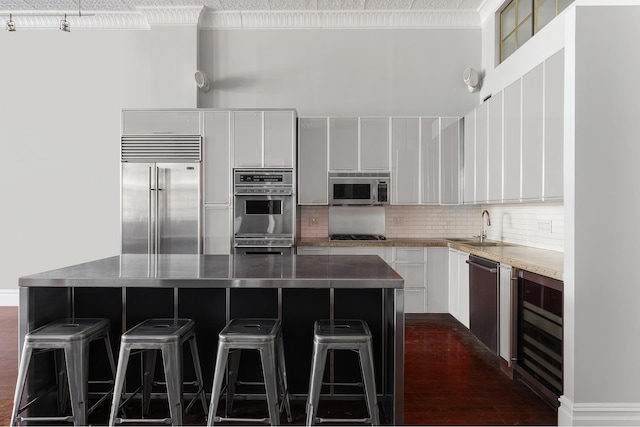 kitchen featuring stainless steel appliances, a sink, a kitchen island, white cabinetry, and decorative backsplash