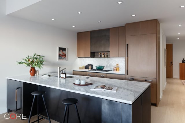 kitchen with sink, a breakfast bar, light stone countertops, stainless steel gas cooktop, and light wood-type flooring