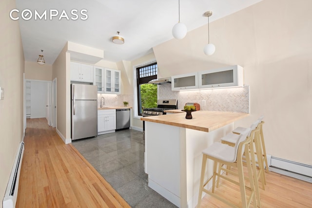 kitchen with white cabinets, a baseboard radiator, glass insert cabinets, decorative light fixtures, and stainless steel appliances