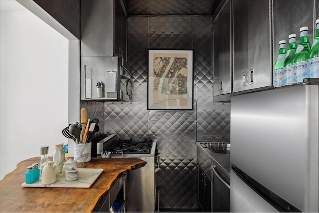 kitchen with butcher block counters, dark cabinetry, backsplash, freestanding refrigerator, and gas range