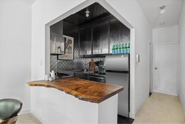 kitchen with dark cabinets, butcher block counters, baseboards, freestanding refrigerator, and decorative backsplash