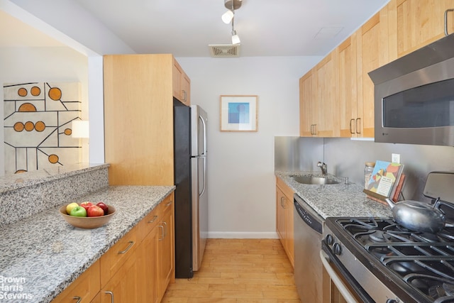 kitchen with light wood finished floors, appliances with stainless steel finishes, light stone counters, and a sink