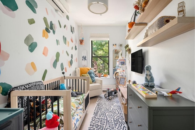 bedroom featuring light wood-style floors, a wall unit AC, and a crib