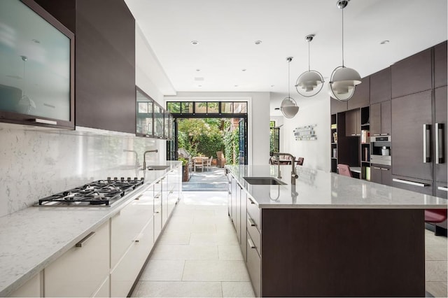 kitchen with decorative backsplash, decorative light fixtures, stainless steel gas stovetop, white cabinetry, and a sink