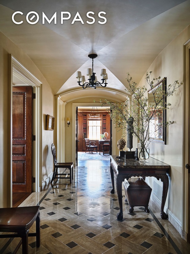 hall featuring a chandelier, arched walkways, baseboards, and lofted ceiling