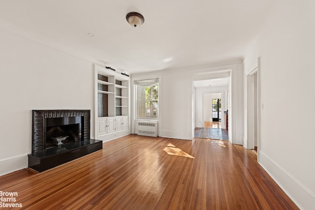 unfurnished living room featuring a fireplace with raised hearth, radiator, baseboards, and hardwood / wood-style floors