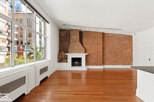 unfurnished living room featuring light wood-type flooring, a fireplace with raised hearth, brick wall, and radiator heating unit