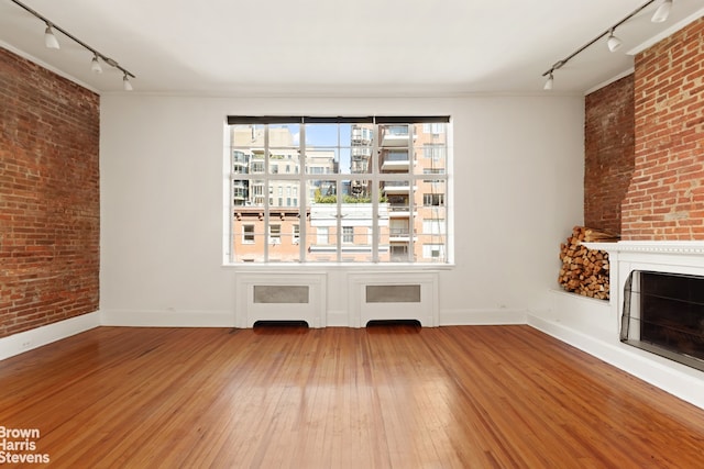 unfurnished living room featuring brick wall, a fireplace, rail lighting, and hardwood / wood-style flooring