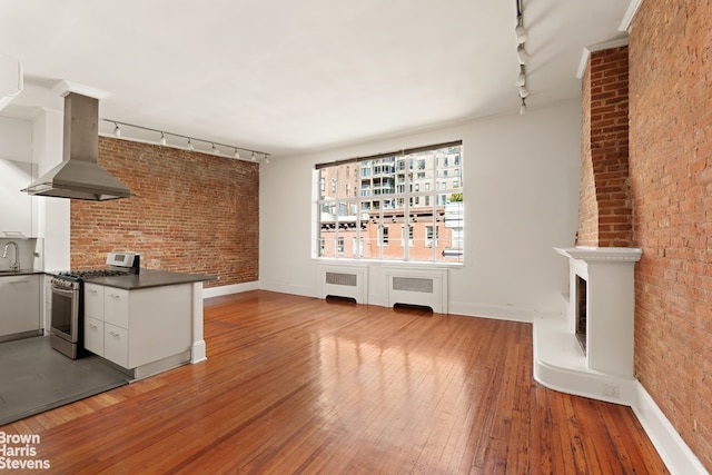 unfurnished living room with rail lighting, radiator, a sink, brick wall, and light wood-style flooring