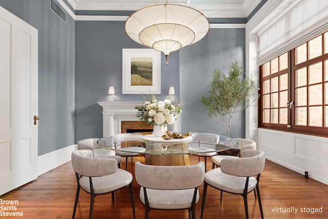dining room featuring crown molding, visible vents, a decorative wall, a fireplace, and wood finished floors