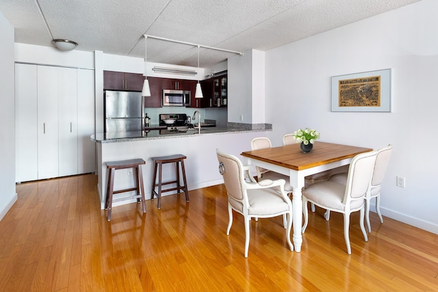 dining area with a textured ceiling, light wood-type flooring, and baseboards