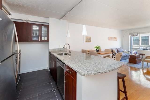 kitchen featuring a peninsula, glass insert cabinets, a kitchen bar, stainless steel appliances, and a sink
