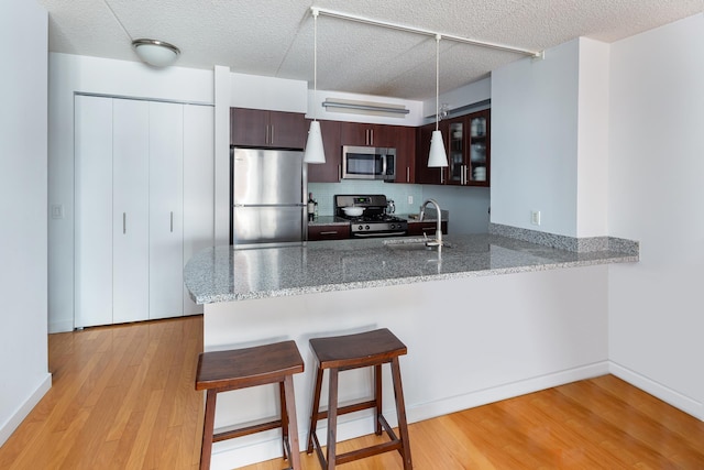 kitchen featuring a peninsula, a sink, a kitchen breakfast bar, appliances with stainless steel finishes, and light wood finished floors