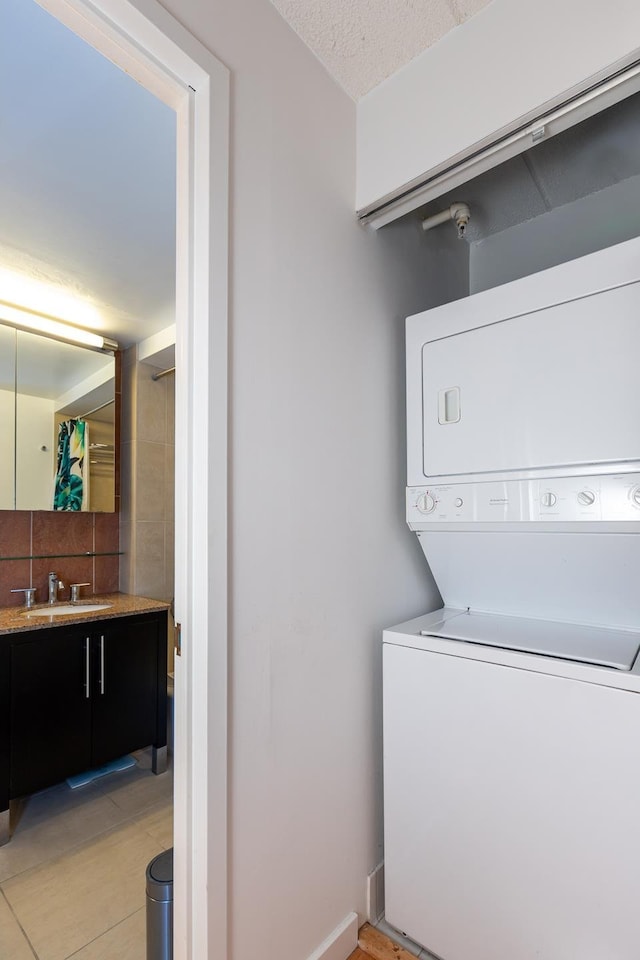 washroom featuring a textured ceiling, light tile patterned floors, laundry area, stacked washer / dryer, and a sink