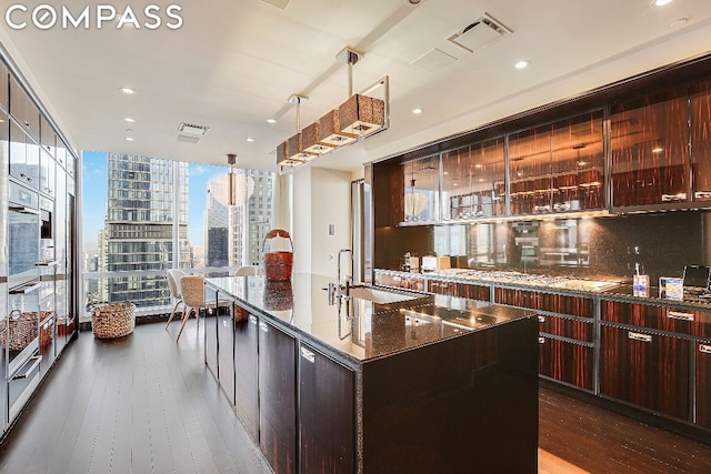 kitchen featuring decorative light fixtures, backsplash, dark wood-type flooring, a large island, and dark stone counters