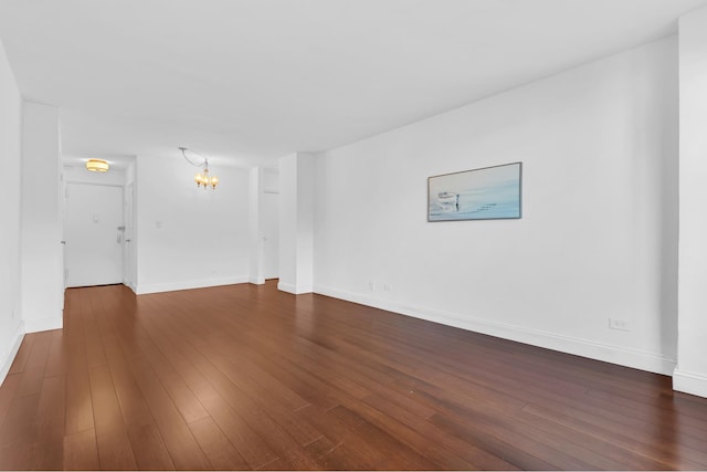 empty room featuring baseboards, a chandelier, and dark wood-type flooring