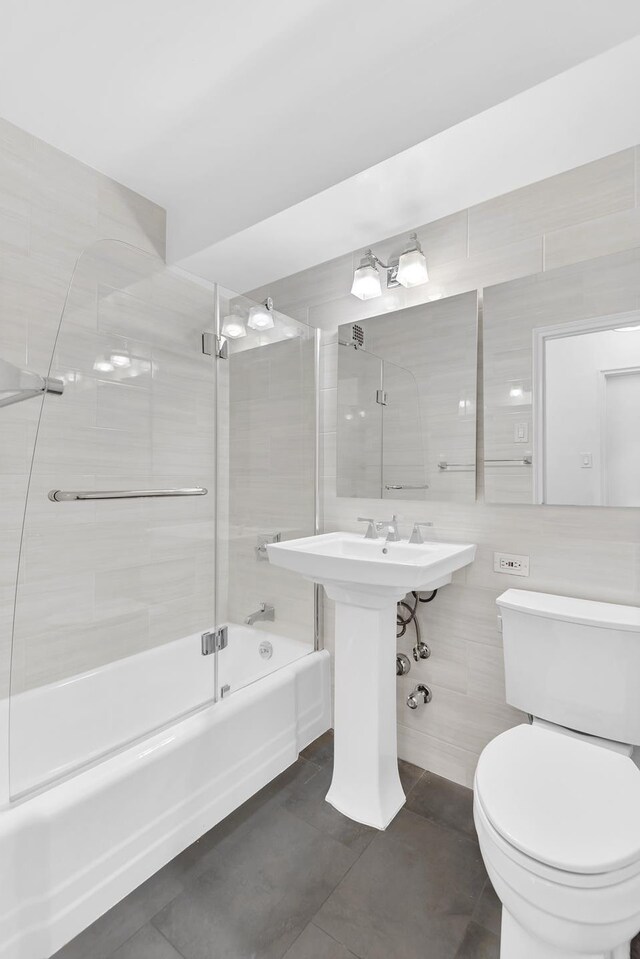 bathroom with tile walls, enclosed tub / shower combo, and toilet