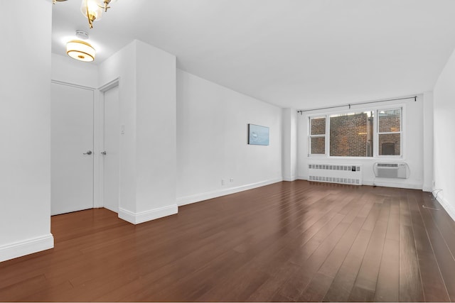 empty room featuring baseboards, dark wood finished floors, a wall unit AC, and radiator heating unit